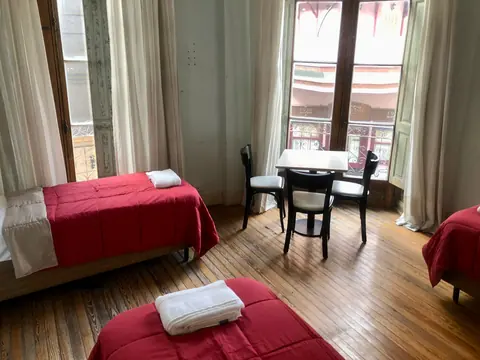Habitación compartida con tres camas, mesa y ventanales al balcón