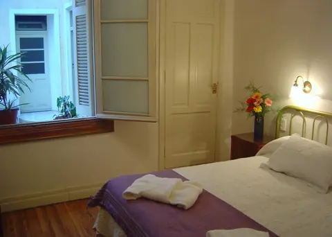 Habitación luminosa con ventana, cama tendida y toallas